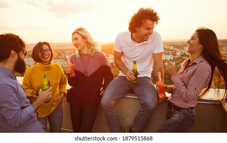 Delighted diverse men and women drinking beer and laughing while talking with each other during evening party on rooftop - Powered by Shutterstock