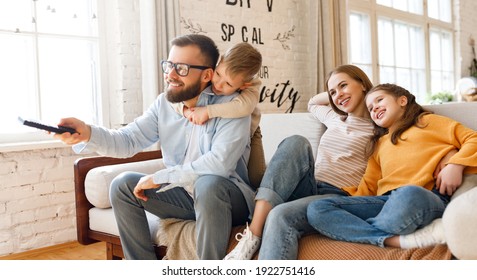 Delighted family parents and kids   smiling while sitting on sofa and watching funny movie on TV at home