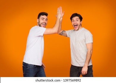 Delighted Friends Giving High Five Gesture Over Orange Background