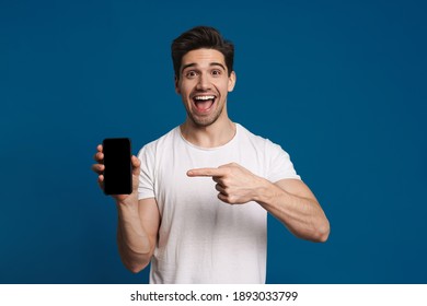 Delighted Guy Showing And Pointing Finger At Mobile Phone Isolated Over Blue Background