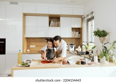 Delighted handsome father teaching daughter hugging applying tomato sauce on prepared rolling dough. Happy family baking cooking pizza in modern kitchen with large window. - Powered by Shutterstock