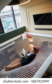 Delighted International Woman Lying On Hammock While Working In The Modern Flex Office