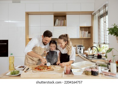 Delighted kid child daughter cutting homemade pizza in pieces wearing aprons. happy parents family spending time together in modern kitchen with large window. - Powered by Shutterstock