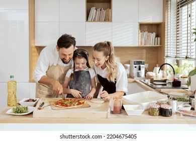 Delighted kid child daughter cutting homemade pizza in pieces wearing aprons. happy parents family spending time together in modern kitchen with large window. - Powered by Shutterstock