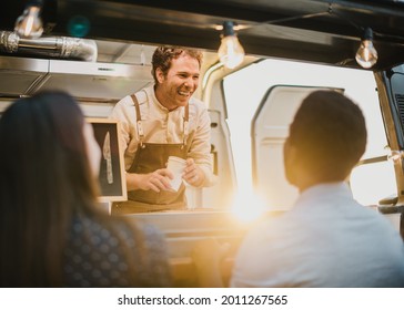 Delighted man with takeaway cups smiling and talking with diverse couple while working in food truck in evening on street - Powered by Shutterstock