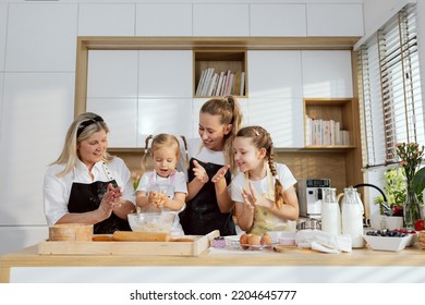 Delighted Mother Granny And Older Daughter Clapping In Hands Supporting Preschooler Girl Kneading Dough In Hands. Family Cooking Baking Homemade Cookies Muffind For Father's Birtday.