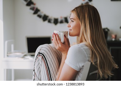 Delighted nice woman resting at home while enjoying her warm drink