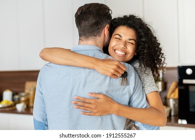 Delighted pleasant young African American woman hugging her boyfriend and feeling thankful for buying a new house, holding keys, and smiling, interracial couple homeowners celebrating the relocation - Powered by Shutterstock