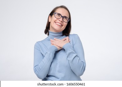 Delighted Pleased Female Coworker Keeps Hand On Chest As Being Satisfied To Hear Compliment From Stranger. Studio Shot