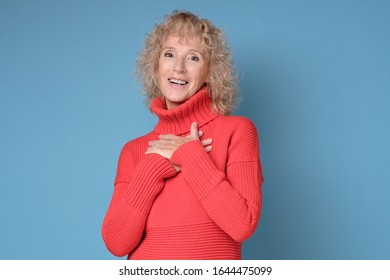 Delighted Pleased Female Teacher Keeps Hand On Chest As Being Satisfied To Recieve Compliment From Stranger. Positive Facial Human Emotion. Studio Shot