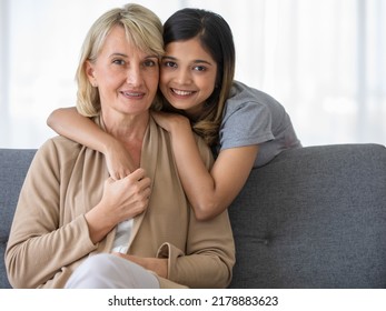 Delighted Young Asian Girl Hugging Happy Middle Aged Foster Mother Sitting On Sofa While Spending Time Together At Home, Adopted Child And Mother In Law Conceppt.