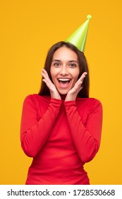 Delighted Young Woman In Bright Clothes Keeping Hands On Cheeks And Screaming After Receiving Surprise During Birthday Party Against Yellow Background