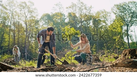 Delightful couple working together during forestation work. Beautiful Caucasian man and cute young woman planting trees with other volunteers. Helping nature and environment.