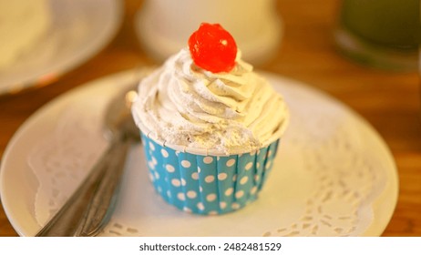 A delightful cupcake in a polka dot wrapper, topped with whipped cream and a cherry, sits on a doily-lined plate with a spoon, ready to enjoy. The scene exudes sweetness and charm. - Powered by Shutterstock