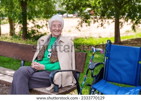 A delightful elderly lady, beaming with happiness, rests on a park bench in a vibrant, leafy city park, basking in the sunny glow after a wheelchair stroll.