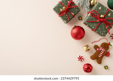 Delightful holiday tableau from top view: emerald gift boxes, red, green, and golden baubles, gingerbread man ornament, jingle bells, candies, frosty fir twig, light background with space for greeting