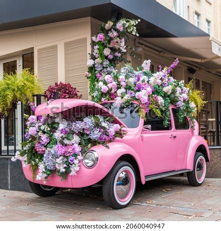 Delightful pink car with huge flowers from the hood in the city.