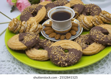 A delightful spread of chocolate-dipped almond cookies and cream-filled biscuits arranged around a coffee cup on a vibrant green plate. Almonds add a touch of elegance. - Powered by Shutterstock