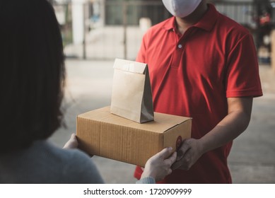 Deliver man wearing face mask in red uniform handling bag and  parcel box give to female costumer Postman and express grocery delivery service during covid19.