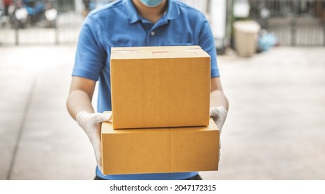 Deliver Man Wearing Medical Gloves And Face Mask In Blue Uniform Handling Parcel Box Give To Female Costumer Postman And Express Grocery Delivery Service During Covid19.