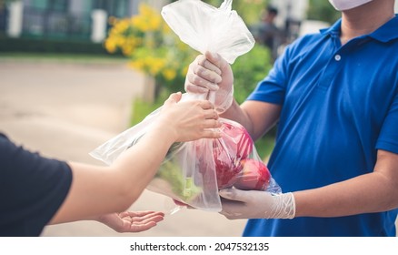 Deliver Man Wearing Medical Gloves And Face Mask In Blue Uniform Handling Bag Of Fruits And Vegetables  Give To Female Costumer Postman And Express Grocery Delivery Service During Covid19.