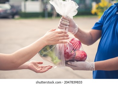 Deliver Man Wearing Medical Gloves And Face Mask In Blue Uniform Handling Bag Of Fruits And Vegetables  Give To Female Costumer Postman And Express Grocery Delivery Service During Covid19.