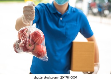 Deliver Man Wearing Medical Gloves And Face Mask In Blue Uniform Handling Apple Bag And Parcel Box Give To Female Costumer Postman And Express Grocery Delivery Service During Covid19.