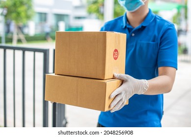 Deliver Man Wearing Medical Gloves And Face Mask In Blue Uniform Handling Parcel Box Give To Female Costumer Postman And Express Grocery Delivery Service During Covid19.