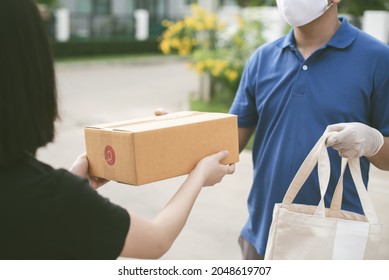 Deliver Man Wearing Medical Gloves And Face Mask In Blue Uniform Handling Bag Of Food And Parcel Box Give To Female Costumer Postman And Express Grocery Delivery Service During Covid19.