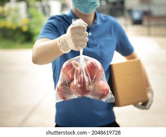 Deliver Man Wearing Medical Gloves And Face Mask In Blue Uniform Handling Apple Bag And Parcel Box Give To Female Costumer Postman And Express Grocery Delivery Service During Covid19.