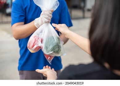 Deliver Man Wearing Medical Gloves And Face Mask In Blue Uniform Handling Bag Of Fruits And Vegetables  Give To Female Costumer Postman And Express Grocery Delivery Service During Covid19.