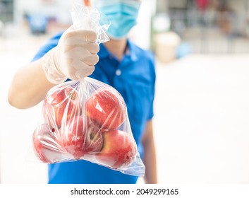 Deliver Man Wearing Medical Gloves And Face Mask In Blue Uniform Handling Apple Bag And Parcel Box Give To Female Costumer Postman And Express Grocery Delivery Service During Covid19.