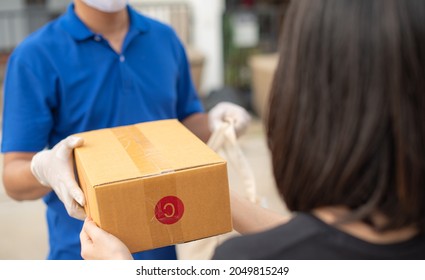 Deliver Man Wearing Medical Gloves And Face Mask In Blue Uniform Handling Bag Of Food And Parcel Box Give To Female Costumer Postman And Express Grocery Delivery Service During Covid19.