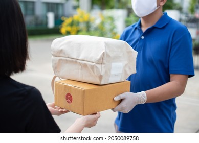 Deliver Man Wearing Medical Gloves And Face Mask In Blue Uniform Handling Bag Of Food And Parcel Box Give To Female Costumer Postman And Express Grocery Delivery Service During Covid19.