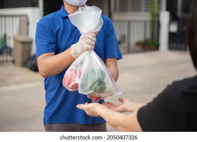 Deliver Man Wearing Medical Gloves And Face Mask In Blue Uniform Handling Bag Of Fruits And Vegetables  Give To Female Costumer Postman And Express Grocery Delivery Service During Covid19.