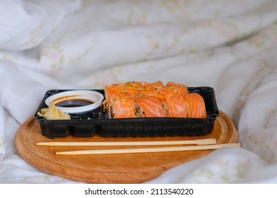 Delivered Sushi With Chopsticks And Plastic Box With Salmon Roll In The Bedroom On Linen. Cozy Home. Eating In Bed. Meal. Traditional Asian Food. Takeout And Delivery. Empty Space.