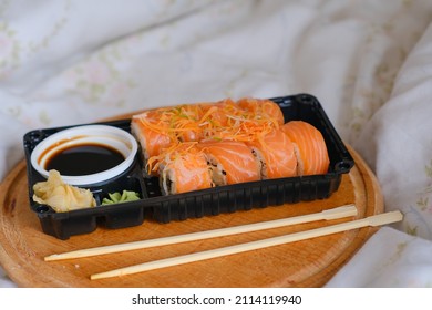 Delivered Sushi With Chopsticks And Plastic Box With Salmon Roll In The Bedroom On Linen. Cozy Home. Eating In Bed. Meal. Traditional Asian Food. Takeout And Delivery. Neutral Interior. Empty Space.