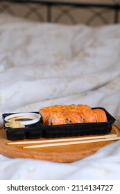 Delivered Sushi With Chopsticks And Plastic Box With Salmon Roll In The Bedroom On Linen. Cozy Home. Eating In Bed. Neutral Bedroom. Meal. Traditional Asian Food. Takeout And Delivery. Empty Space.