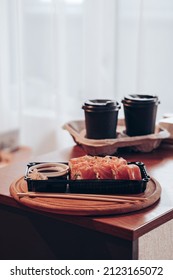 Delivered Sushi With Chopsticks And Plastic Box With Salmon Roll With Two Cups Of Coffee On A Table. Cozy Home. Eating At The Kitchen. Meal. Traditional Asian Food. Takeout And Delivery.