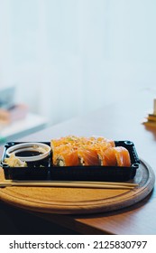 Delivered Sushi With Chopsticks And Plastic Box With Salmon Roll On A Table. Cozy Home. Eating At The Kitchen. Meal. Traditional Asian Food. Takeout And Delivery.