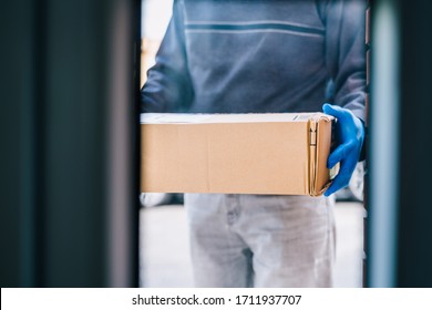 Deliverer Leaving A Package At The Customer's Door As A Measure Of Protection Against The Coronavirus. Delivering A Package To A House With Blue Latex Gloves. Delivery Man Through The Glass Door.