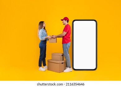 Delivery App. Male Courier Near Big Smartphone Screen Giving Cardboard Parcel Box To Female Customer Standing In Studio Over Yellow Background. Technology And Transportation. Mockup, Full Length