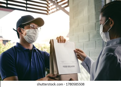 Delivery Of An Asian Man Handing A Bag Of Food To A Female Customer At The Door While Wearing A Protective Mask During A Virus Epidemic.