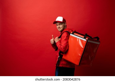 Delivery boy with red thermal bag showing a thumb up. Fast and convenient food delivery service for self-isolated citizens during an epidemic of viral disease. Boy delivering food to customers. - Powered by Shutterstock