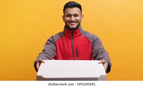 Delivery boy wearing uniform holding pizza box in his hand. Concept of home delivery services during Covid-19. Isolated man smiling with yellow background studio.