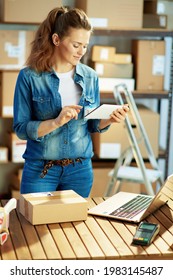 Delivery Business. Happy Modern Woman In Jeans With Parcels Using Tablet PC Applications In The Warehouse.