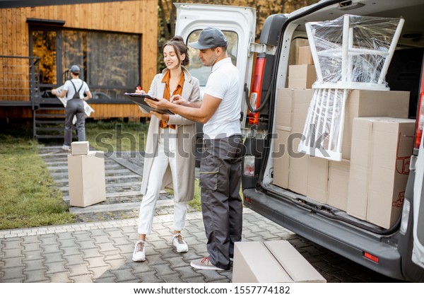 Delivery company employees unloading goods from\
a car trunk, delivering goods to a woman\'s home. Happy client\
signing delivery\
documents