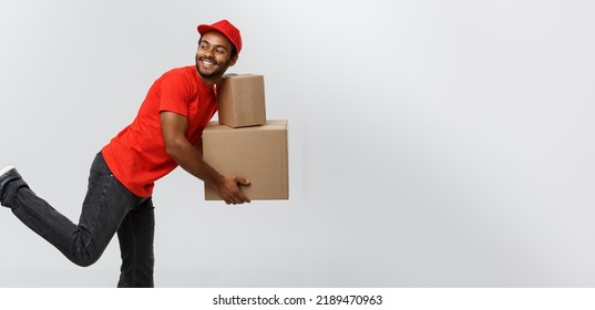 Delivery Concept - Handsome African American Delivery Man Rush Running For Delivering A Package For Customer. Isolated On Grey Studio Background. Copy Space.