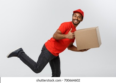 Delivery Concept - Handsome African American Delivery Man Rush Running For Delivering A Package For Customer. Isolated On Grey Studio Background. Copy Space.