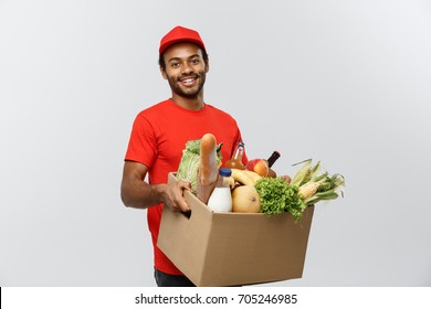 Delivery Concept - Handsome African American delivery man carrying package box of grocery food and drink from store. Isolated on Grey studio Background. Copy Space. - Powered by Shutterstock